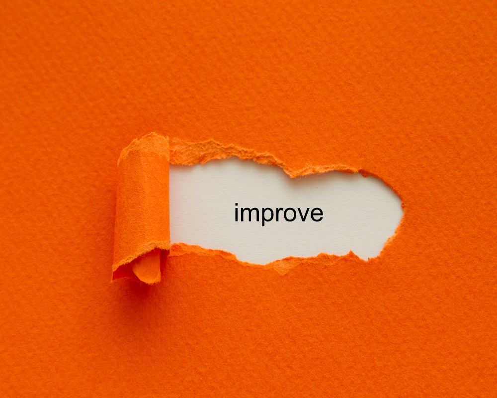 Orange paper ripped to reveal the words improve