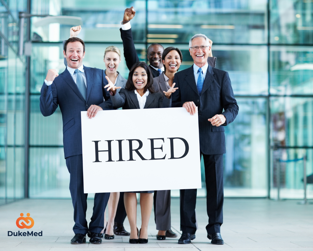 Excited business team holding a ‘HIRED’ sign, celebrating successful recruitment and team-building.