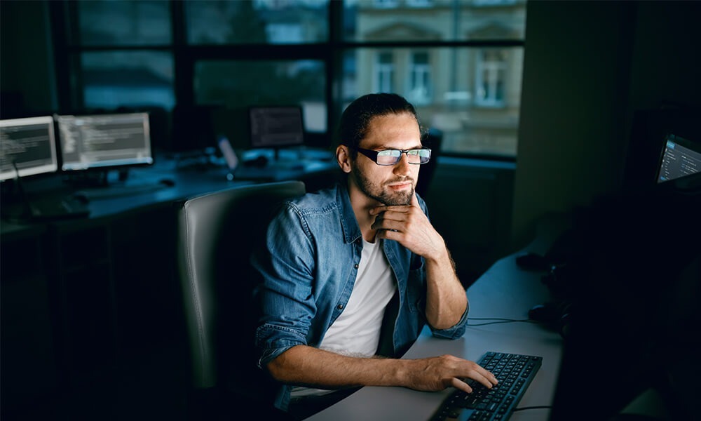 IT contractor analyzing computer screen wearing a demin shirt, with reflection in glasses