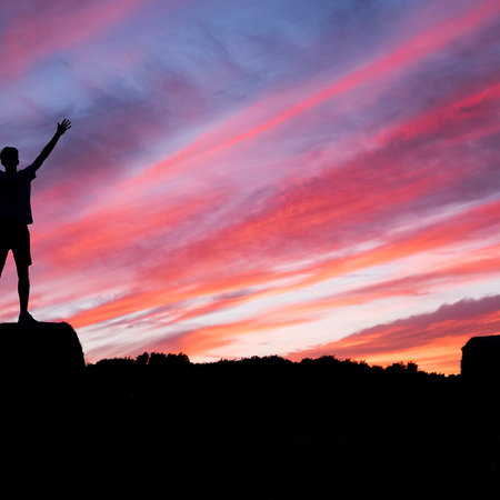Silhouette of man standing on rock with arms in the air