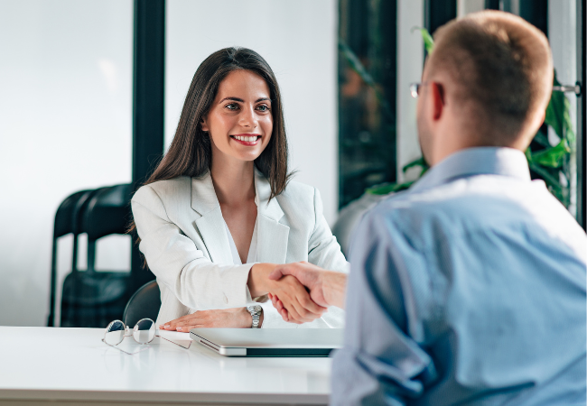 Woman shaking hands with a man across desk. 
