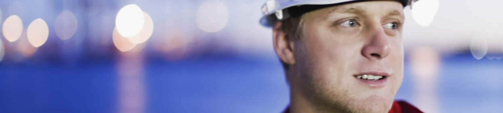 Man in a safety helmet with blurred lights in the background.