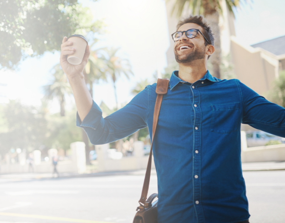 An excited person raising arms with coffee cup in one hand.