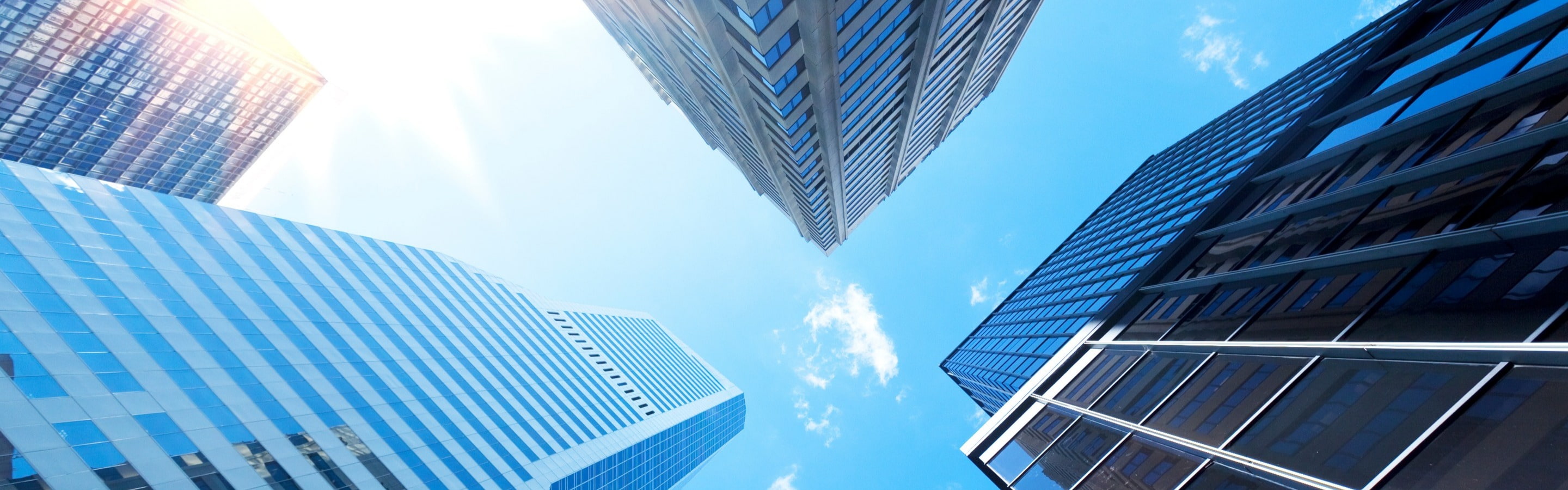 Four high rise buildings in a city with reflection of blue sky bouncing off windows