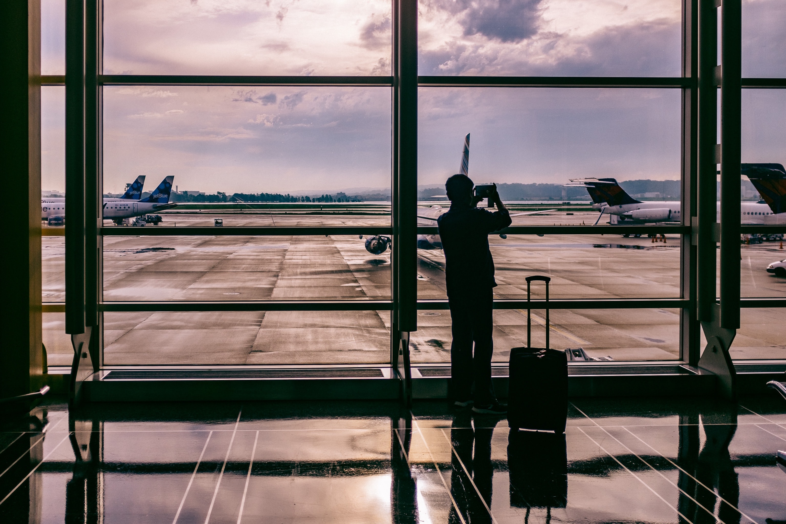 Traveller with suitcase taking photo of airport tarmac