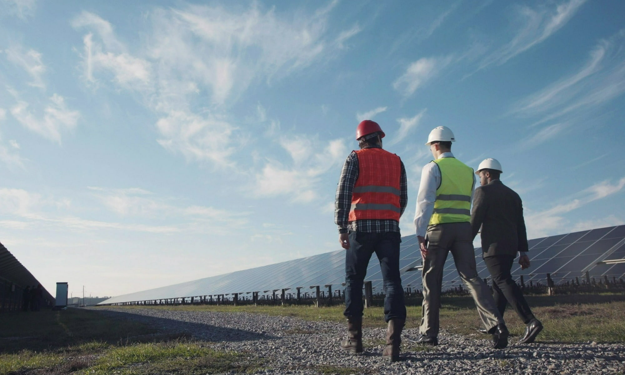 Three workers walking past a solar panel farm.