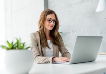 Woman with glasses typing on a laptop.