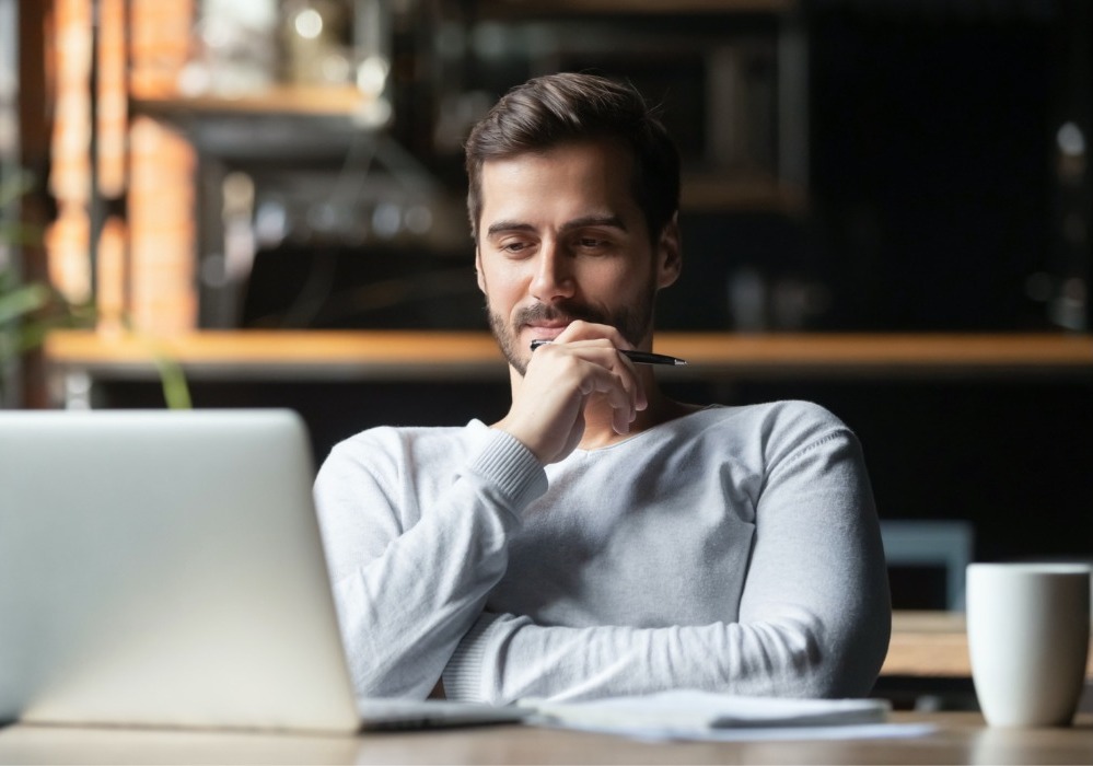 Guy at a cafe on his laptop thinking