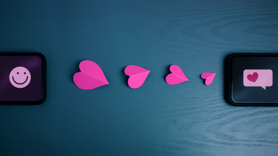 A sequence of pink paper hearts placed between two smartphones, one displaying a smiley face and the other a heart message icon. Symbolizing digital connections, communication, and the matchmaking process in hiring and job searching.