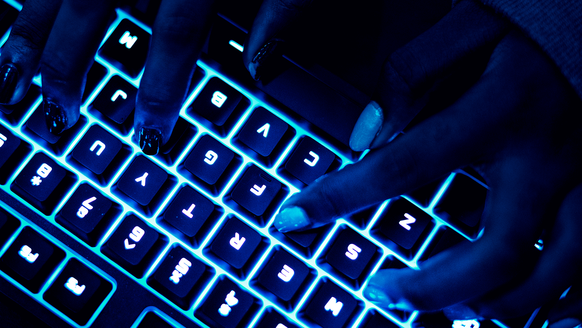 Glowing blue lights illuminate a keyboard as hands with manicured nails type away in a dark setting, evoking a sense of modern technology in use.