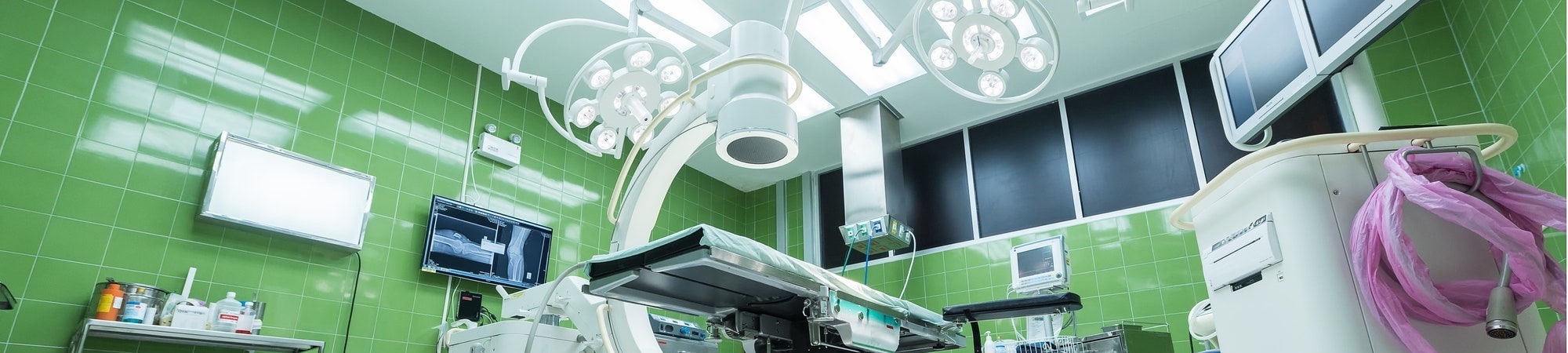 Modern operating theatre with green tiled walls and advanced medical equipment in the foreground 