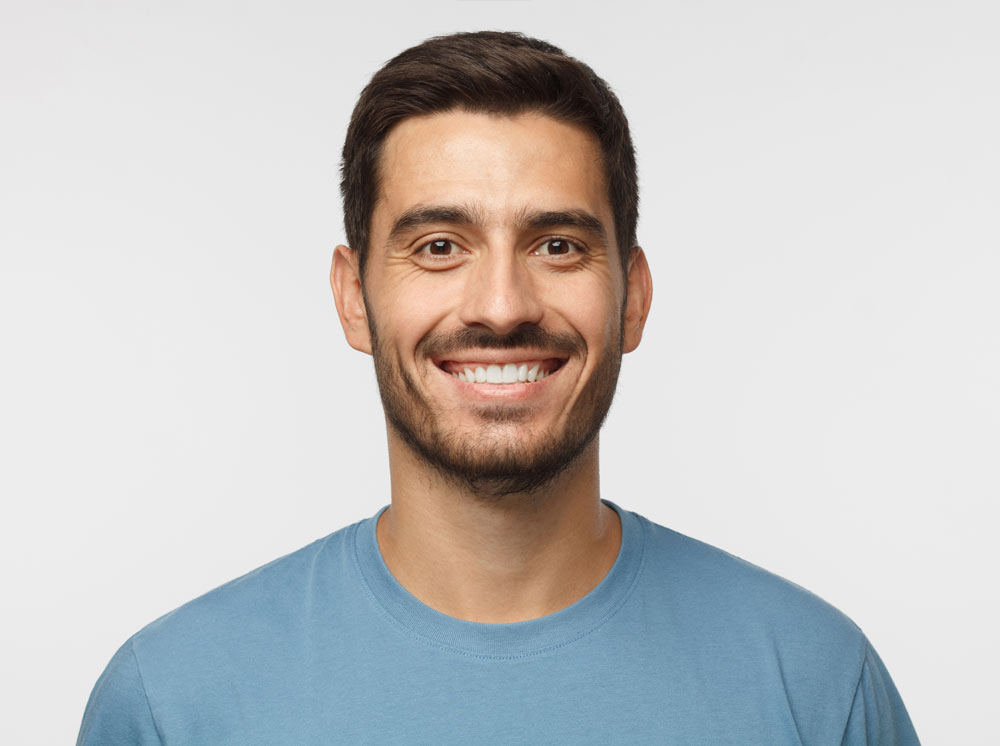 Close Up Portrait Of Young Smiling Handsome Guy In Blue T Shirt Isolated On Gray Background