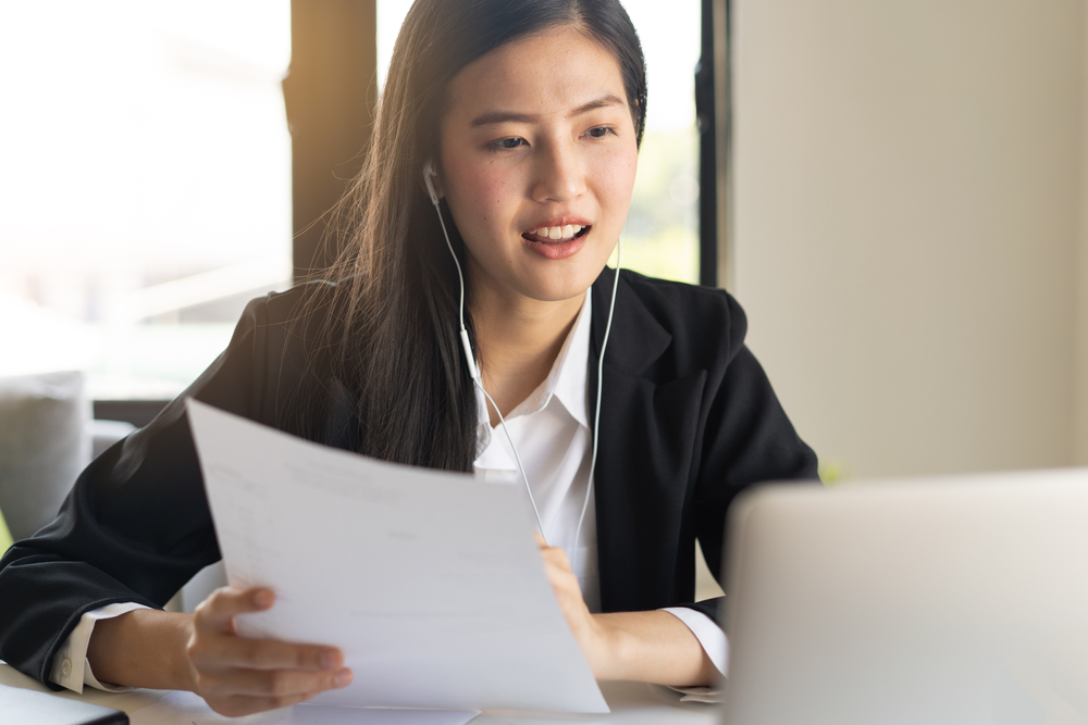 Asian young business woman holding paperwork and video calling via laptop