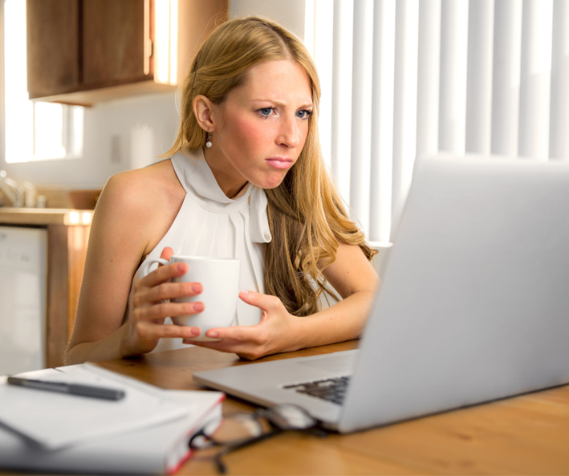 Frustrated woman holding a coffee cup while looking at a laptop, symbolising the challenge of not receiving responses from job applications.