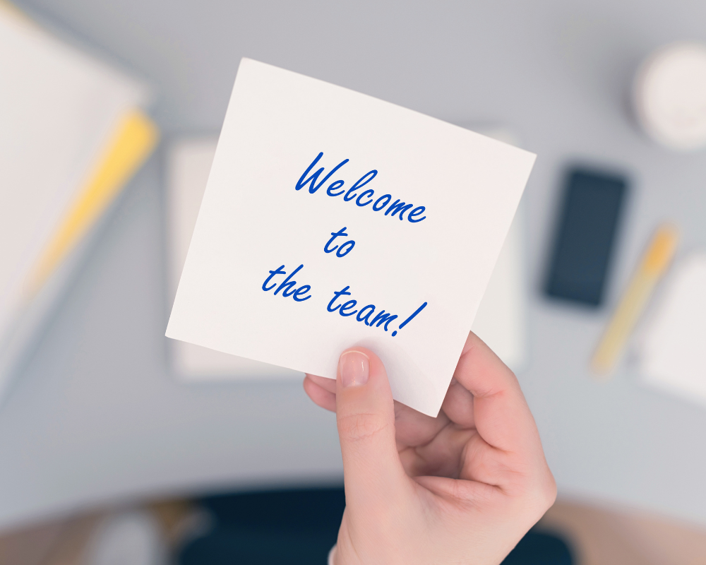 A person holding a post it with the words welcome to the team