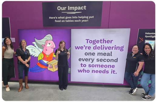 inside the foodbank warehouse group of people smiling infront of poster