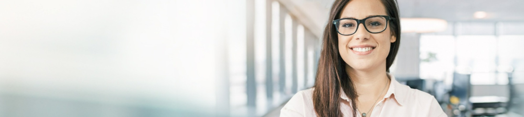 Woman wearing glasses smiling in a modern office environment.