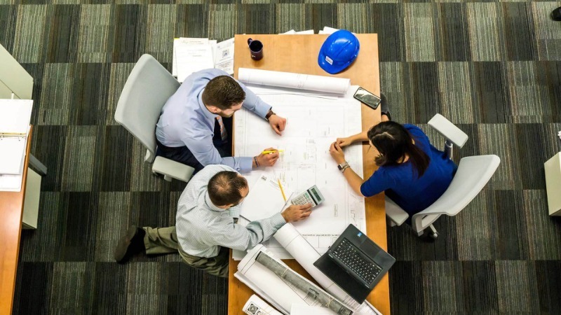 Three Workers Communicating Around a Table in the Construction Industry