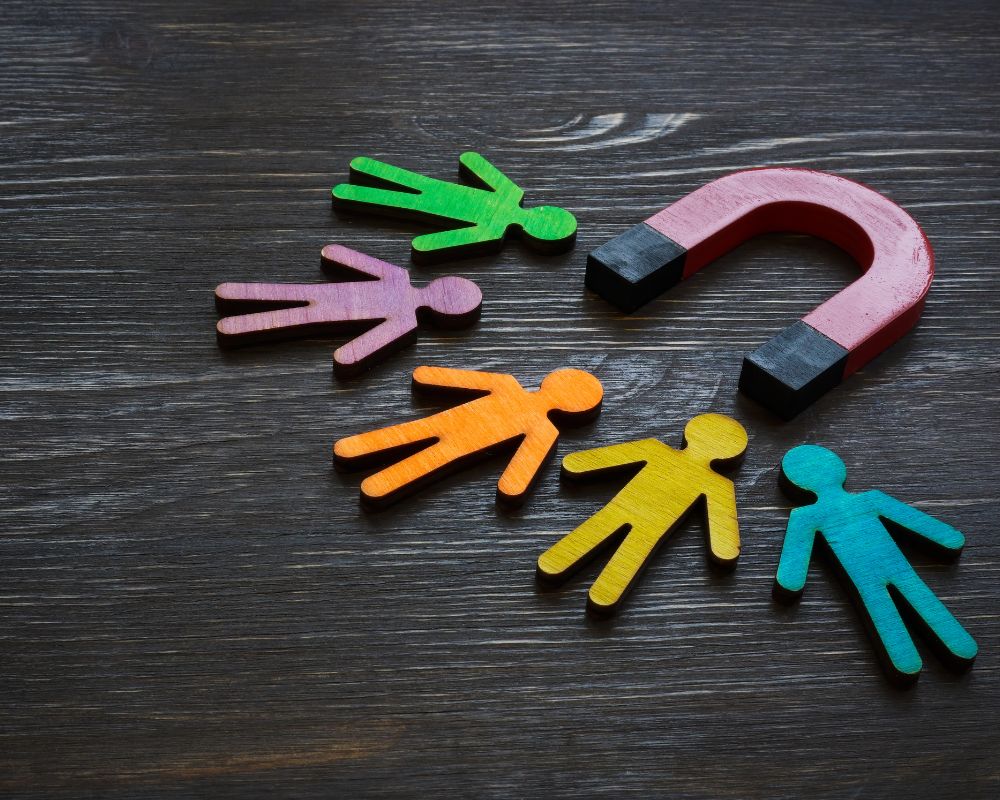 A red horseshoe magnet attracting colorful wooden human-shaped figures on a dark wooden surface, symbolizing the strategic pull of retained search in attracting top MedTech talent.