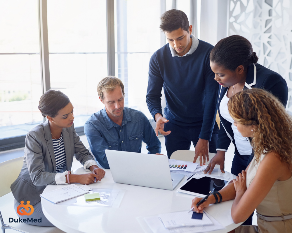 A diverse group of professionals discussing strategy around a laptop, symbolising talent intelligence and collaboration.