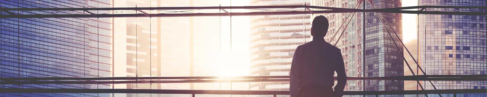 Person with glasses staring off into the sunset from a high-rise building