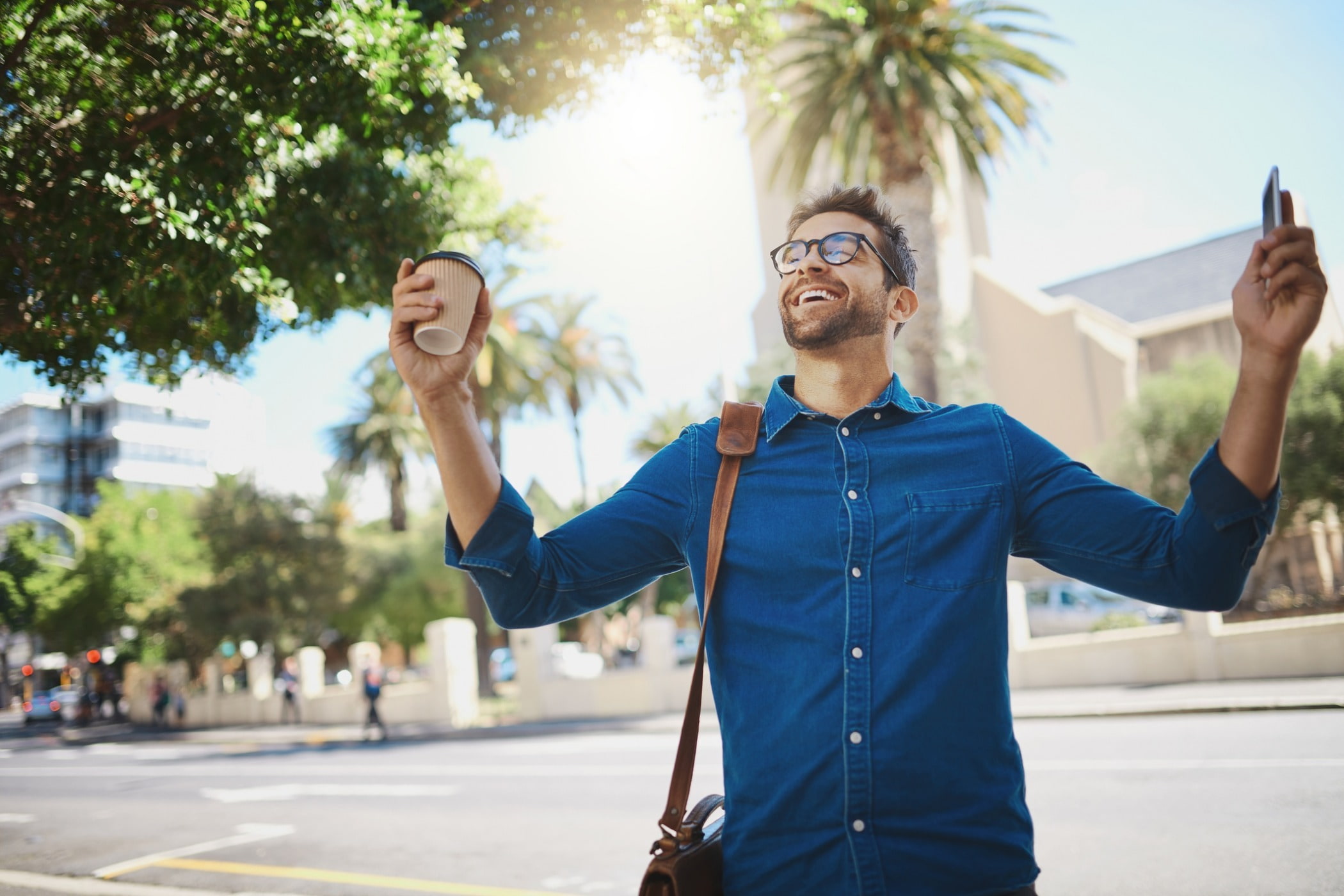 An excited person raising arms with coffee cup in one hand.