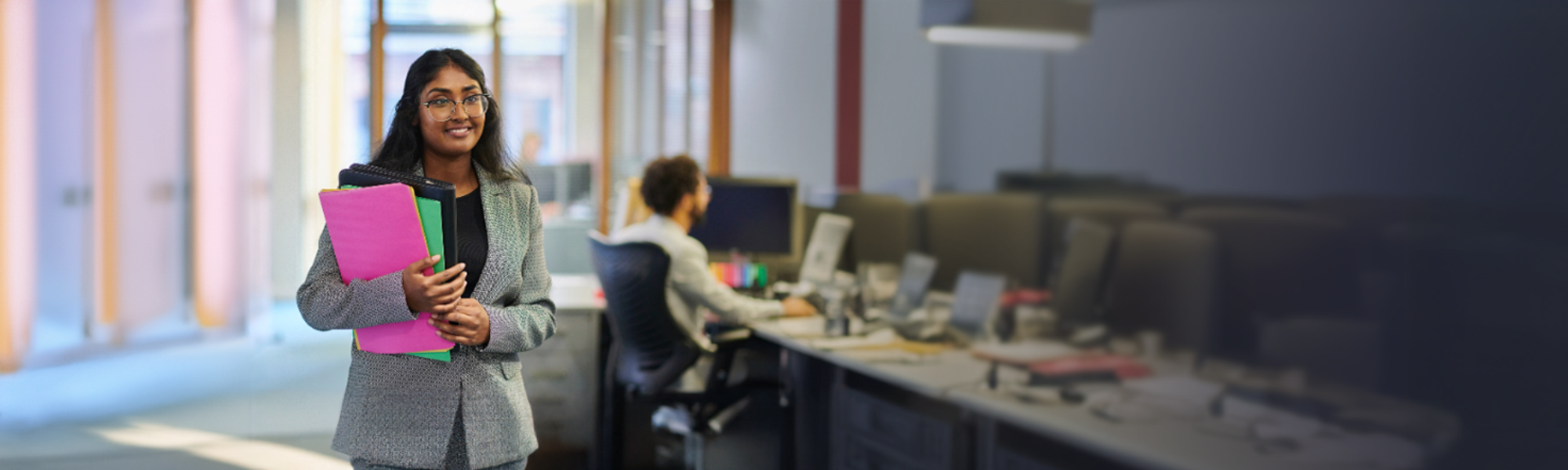 Lady with glasses, holding files and walking through an office