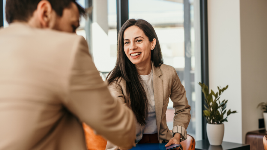 rofessional businesswoman smiling and shaking hands in a modern office setting, representing a successful job interview or career opportunity.