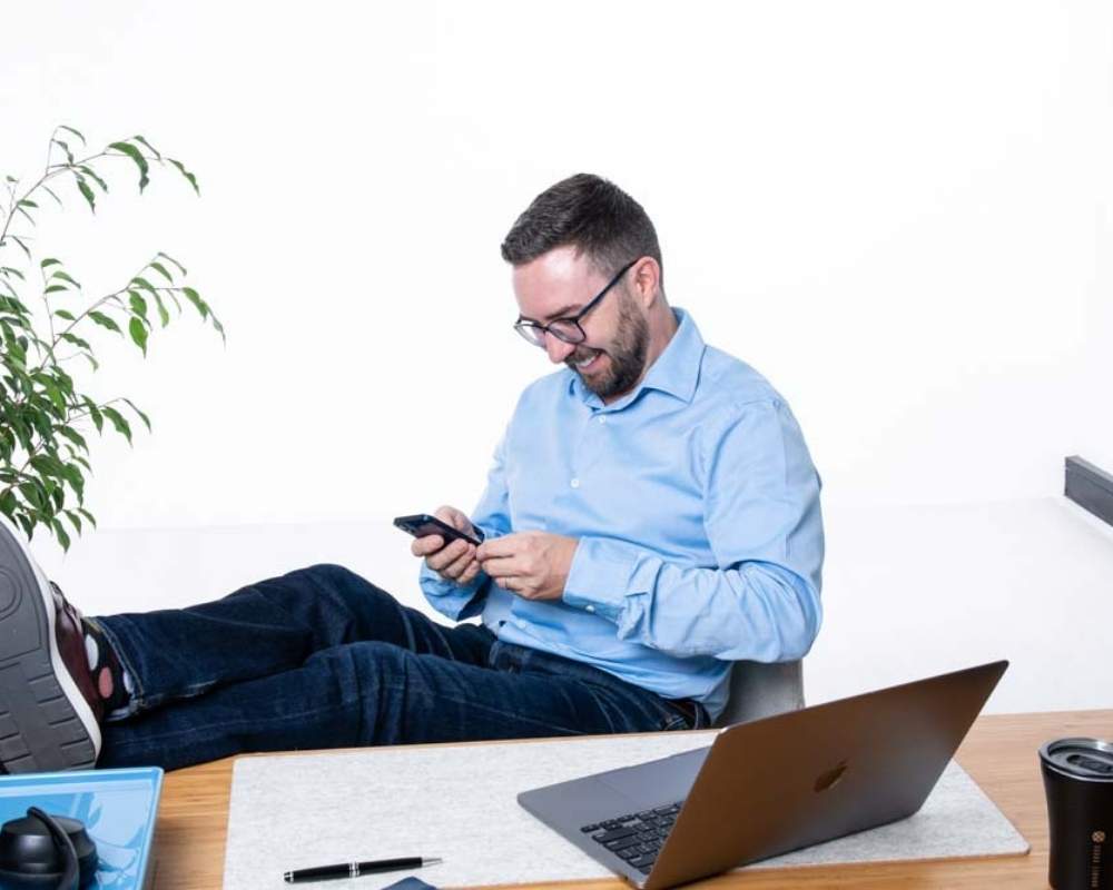 Man sitting at his desk with feet up looking at his mobile.