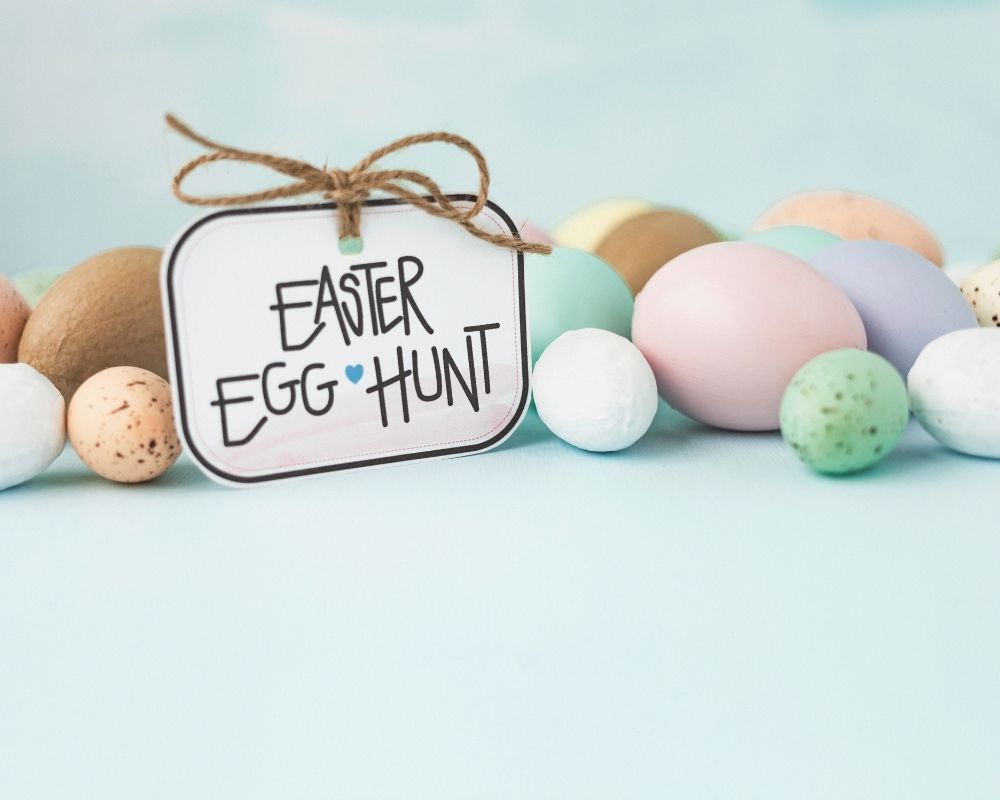 Easter egg hunt sign on a blue background surrounded by easter eggs.