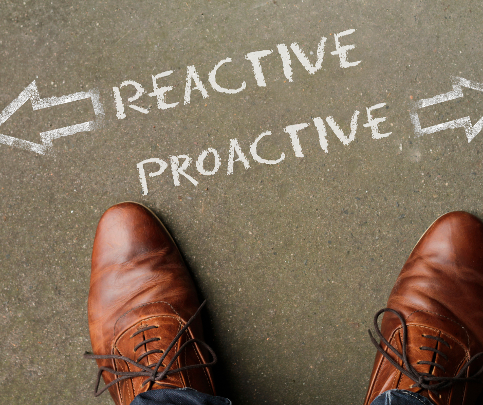 A pair of brown shoes standing on a concrete floor with arrows pointing in opposite directions, labeled ‘Reactive’ and ‘Proactive’, symbolizing a choice in approach.