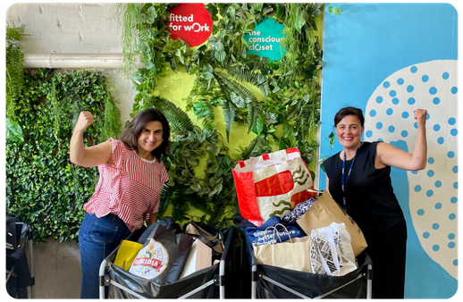 two women posing with strong arms next to a donation box of clothing