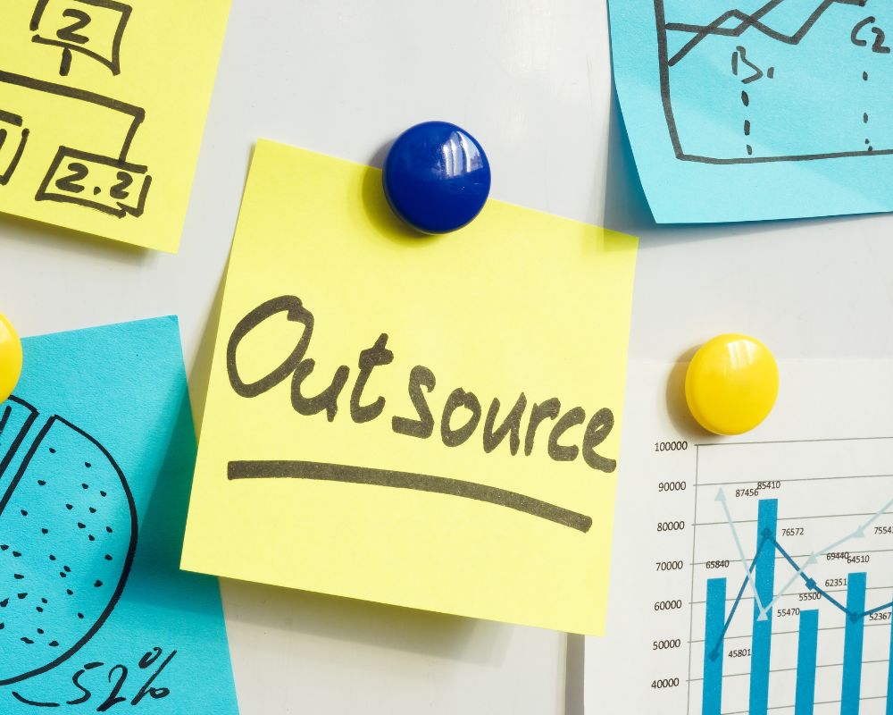 Outsource written on a yellow post it note 