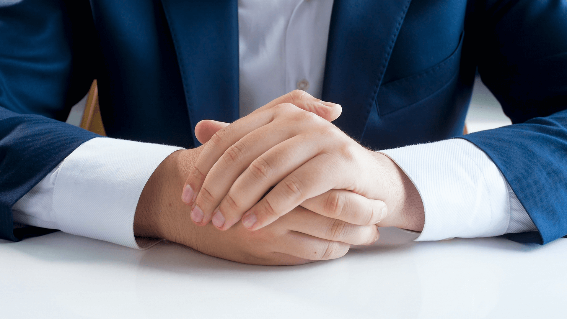 A professional demeanor: a person in a blue suit with hands clasped together on a desk, conveying readiness and confidence.