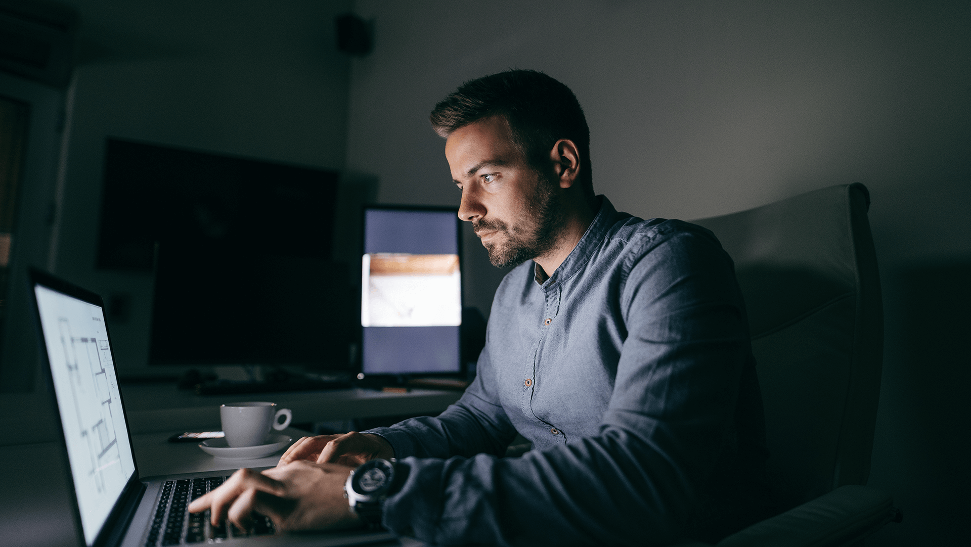 Focused man working late at night in a home office illuminated by the soft glow of computer screens.