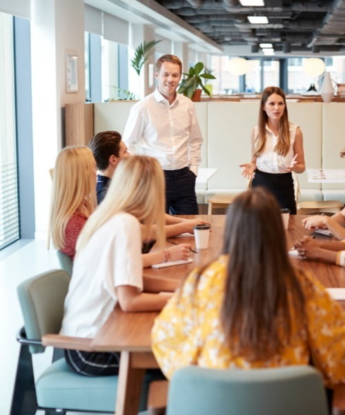 Group Of Young Candidates Sitting At Boardroom Table Applauding Presentation At Business Graduate Recruitment Assessment Day