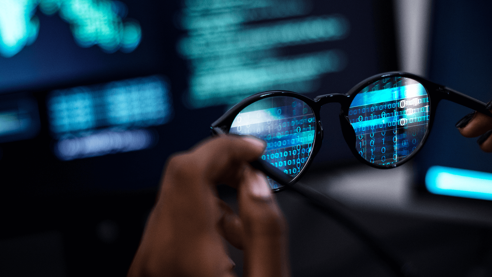 A close-up of a hand holding eyeglasses through which digital binary code is reflected, symbolizing a clear focus on technology and data.