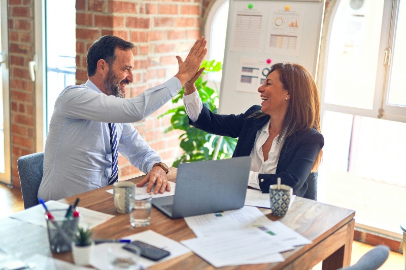 male and female colleagues high fiving over a laptop in an office 