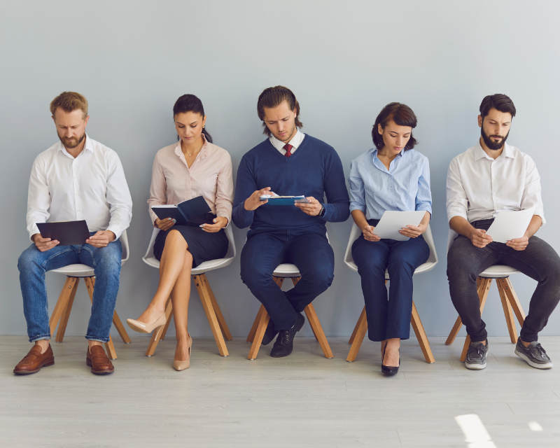 Group of diverse candidates sitting in a waiting area, preparing for interviews, representing the recruitment process.