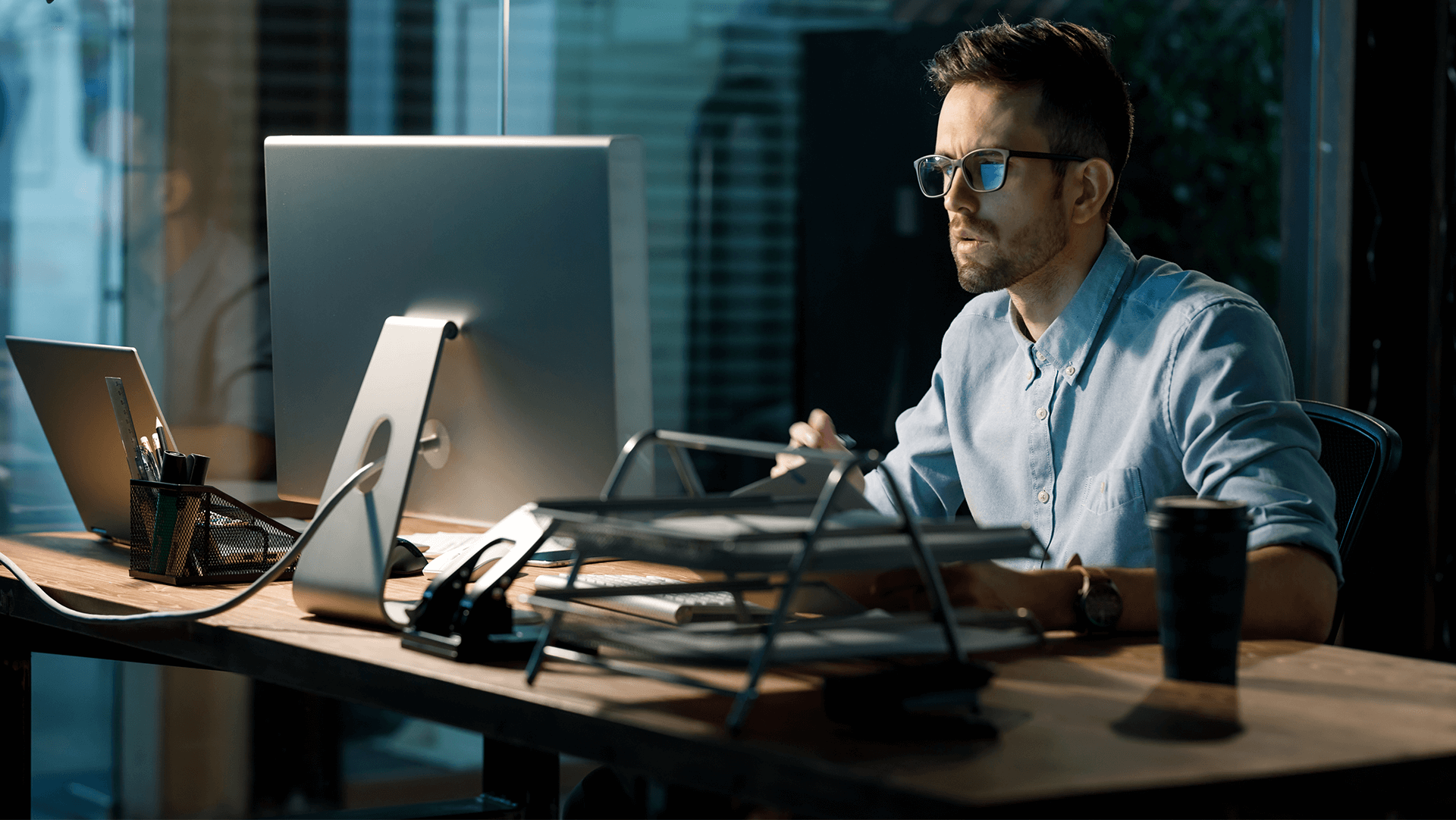 Focused professional working late hours at a modern office setup with multiple screens and devices.