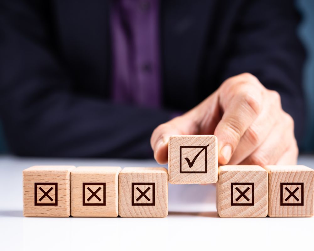 A business professional placing a wooden block with a checkmark among blocks with “X” symbols, symbolizing the effectiveness of retained search in improving hiring outcomes.l