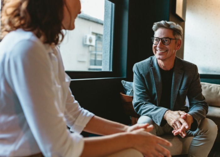 Two work colleagues seated having a conversation by a window. 